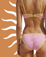 Back view of a pink bikini bottom with yellow trim against a brown background